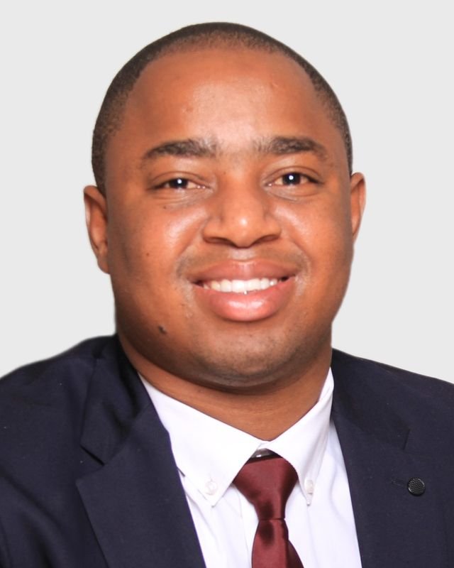 Frank Tsuro in a navy suit, white shirt and maroon tie, facing the camera. Studio headshot in colour.