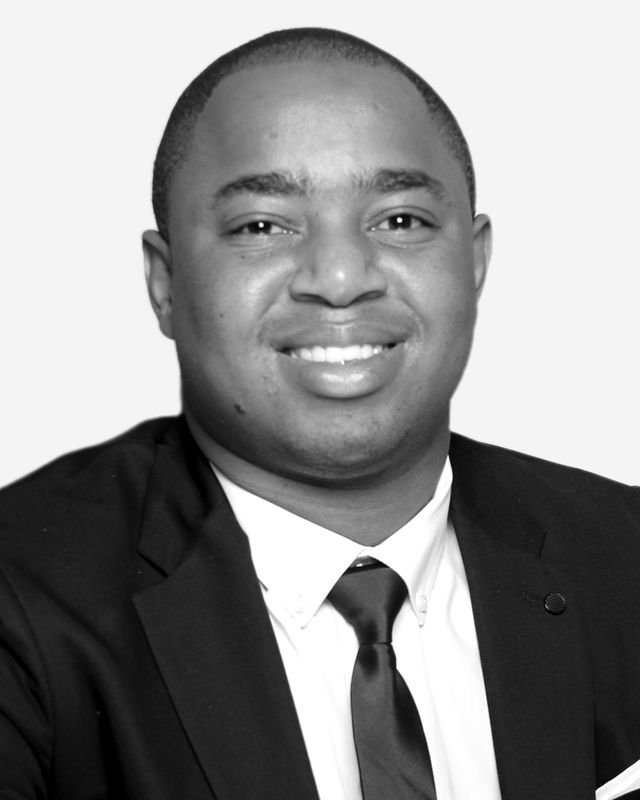 Frank Tsuro in a suit and tie, facing the camera. Studio headshot in black and white.
